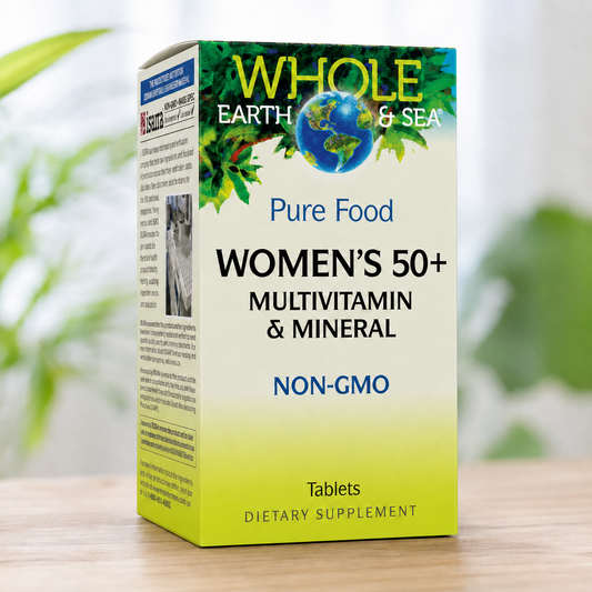 A box of Whole Earth & Sea Women's 50+ Multivitamin & Mineral dietary supplement, standing on a light wooden surface with a blurred green plant in the background.