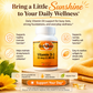 A bottle of Betty's Bakes Vitamin D-3 dietary supplement centered on a warm yellow and orange promotional background with sun graphics, icons, and text highlighting benefits. The bottle is white with a yellow label, and the scene includes decorative leaves, a flower, and softgels.