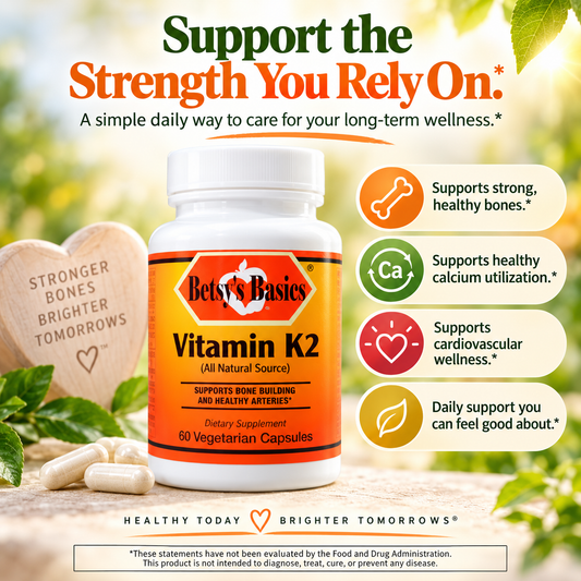 Betsy's Basics Vitamin K2 dietary supplement bottle on a bright, sunny outdoor-style background with green leaves and beige stones. The bottle is white with an orange label.