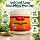 A jar of Betsy's Basics Organic Greens Powder dietary supplement centered on a wooden surface, surrounded by marketing callouts and fresh greens. The product label is orange and white with red accents, and the background is a soft-focus green outdoor scene.
