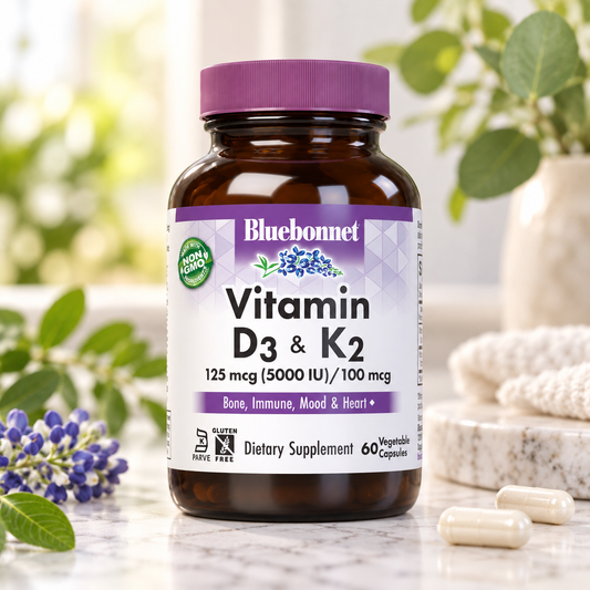 A bottle of Bluebonnet Vitamin D3 & K2 dietary supplement, 60 veggie capsules, set on a marble surface with blurred green leaves and purple flowers in the background.