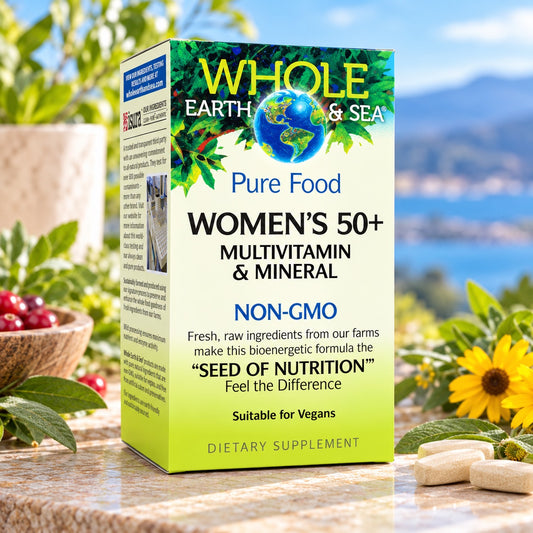 A box of Whole Earth & Sea Women's 50+ Multivitamin & Mineral dietary supplement, standing on a light wooden surface with a blurred green plant in the background.